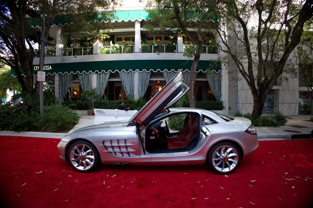 Silver luxury sports car parked on red carpet outside a stylish building with greenery.