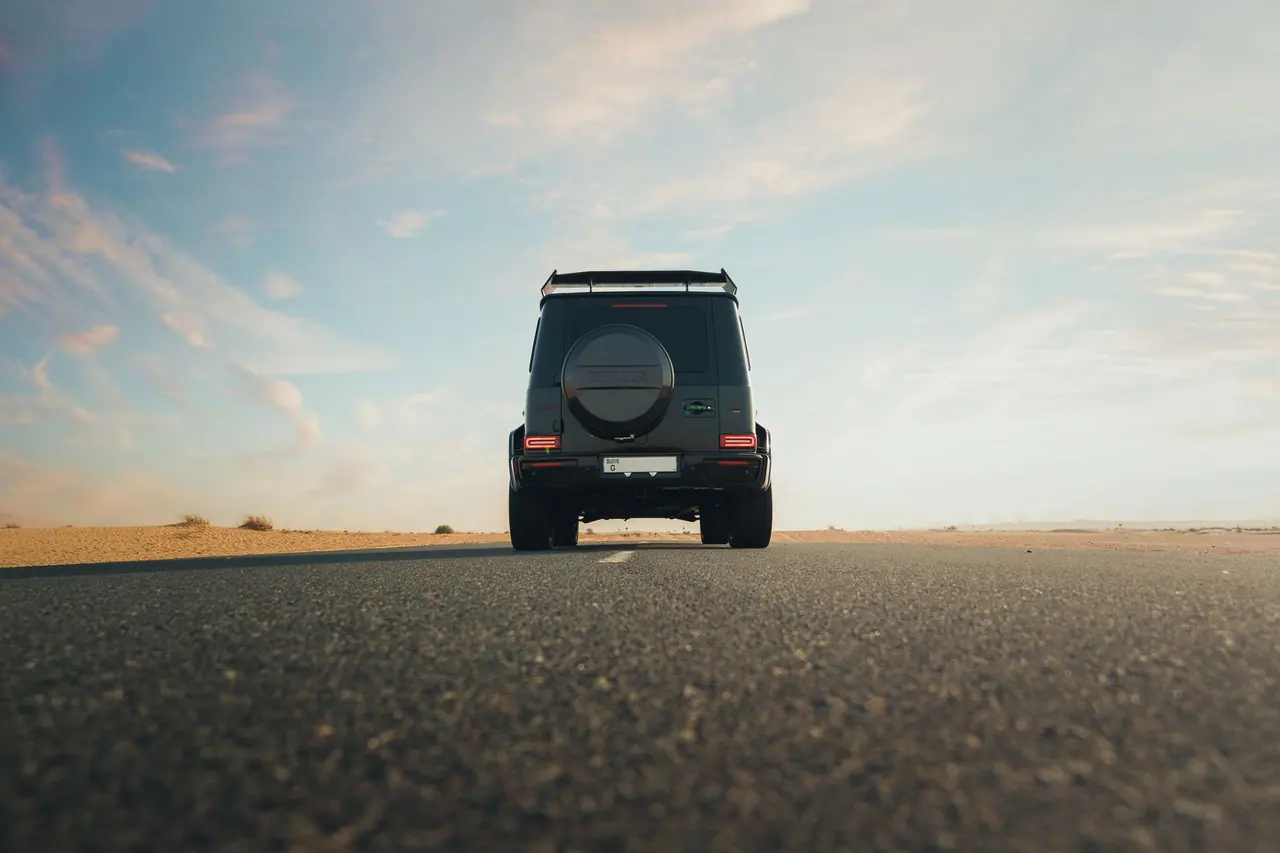A luxury SUV driving along a deserted roadway under a clear blue sky in the desert.