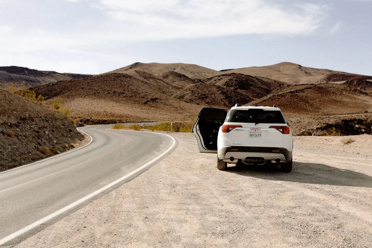 White SUV parked along a winding desert road under clear skies, showcasing adventure and travel.